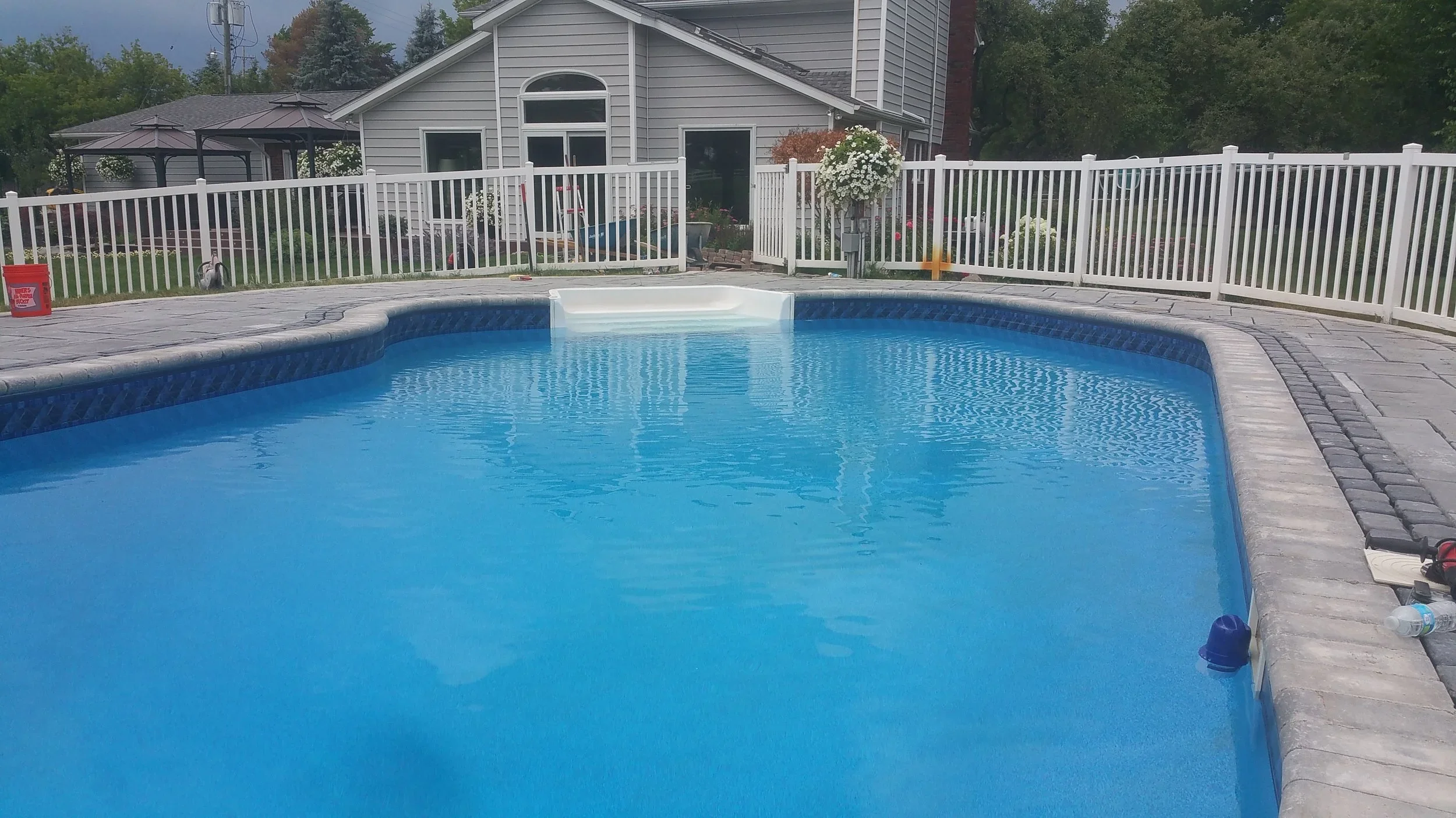 Residential pool landscaping with backyard swimming pool, white fence, trees, and outdoor living area.