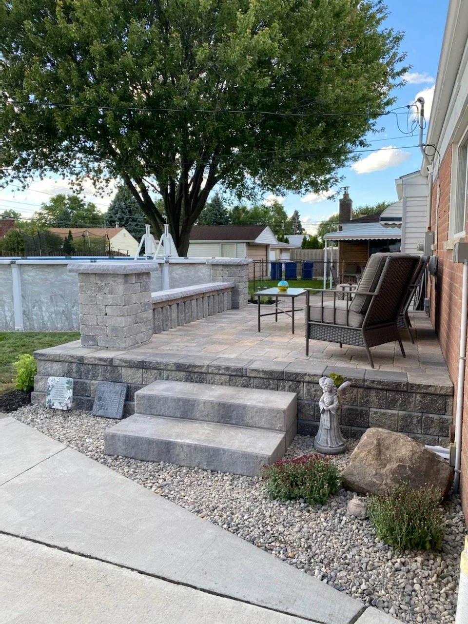 Raised patio installing with gray stone steps, outdoor seating, gravel landscaping, and decorative garden features.