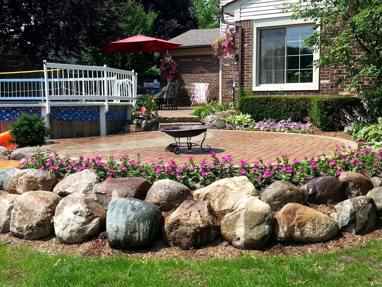 Brick paver patio with fire pit, natural boulder wall and pink flower bed at a Macomb County home