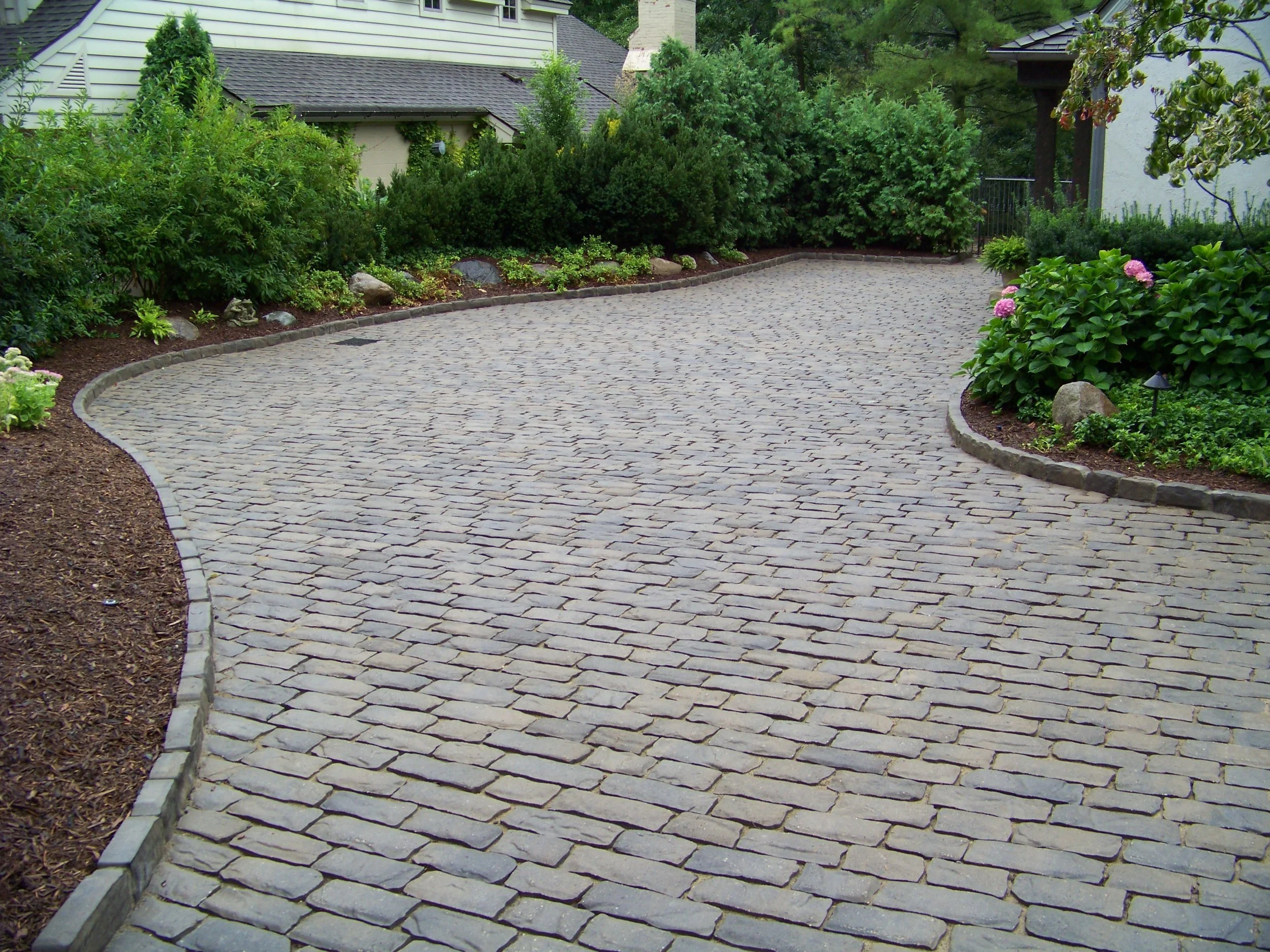 Custom paver driveway with professional landscape edging, mulch beds, shrubs, and clean hardscape design for a polished outdoor entrance.