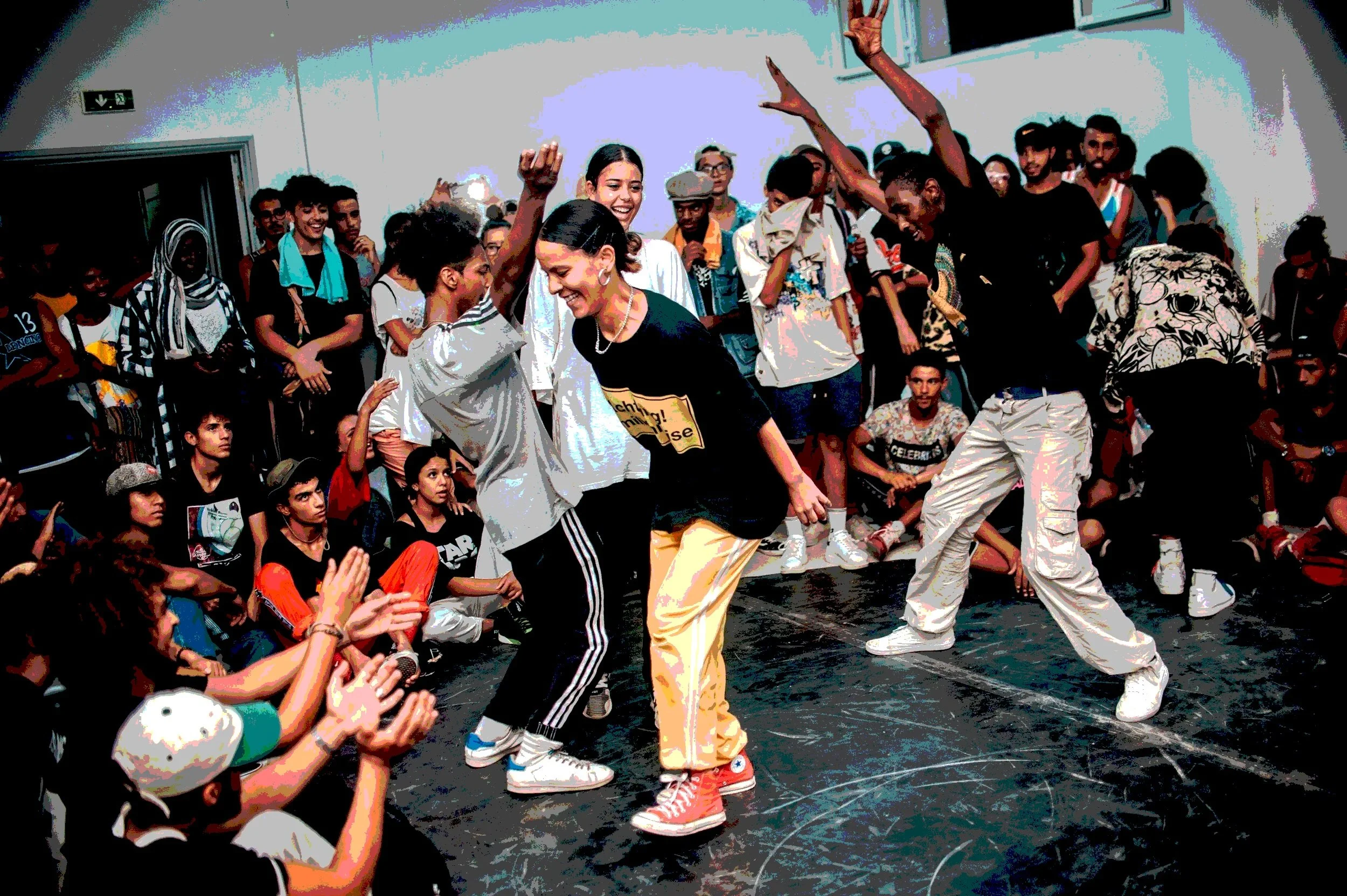 Group of people dancing at an indoor event, some standing and dancing while others watch intently nearby, community joyfully gathered together