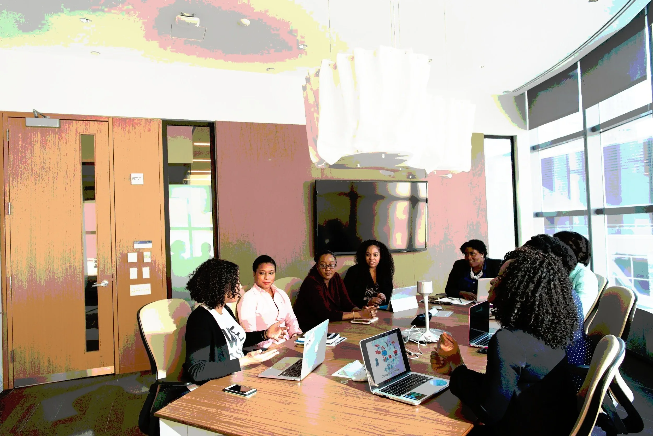 Team of Black women collaborating around a table with laptops, discussing research strategy