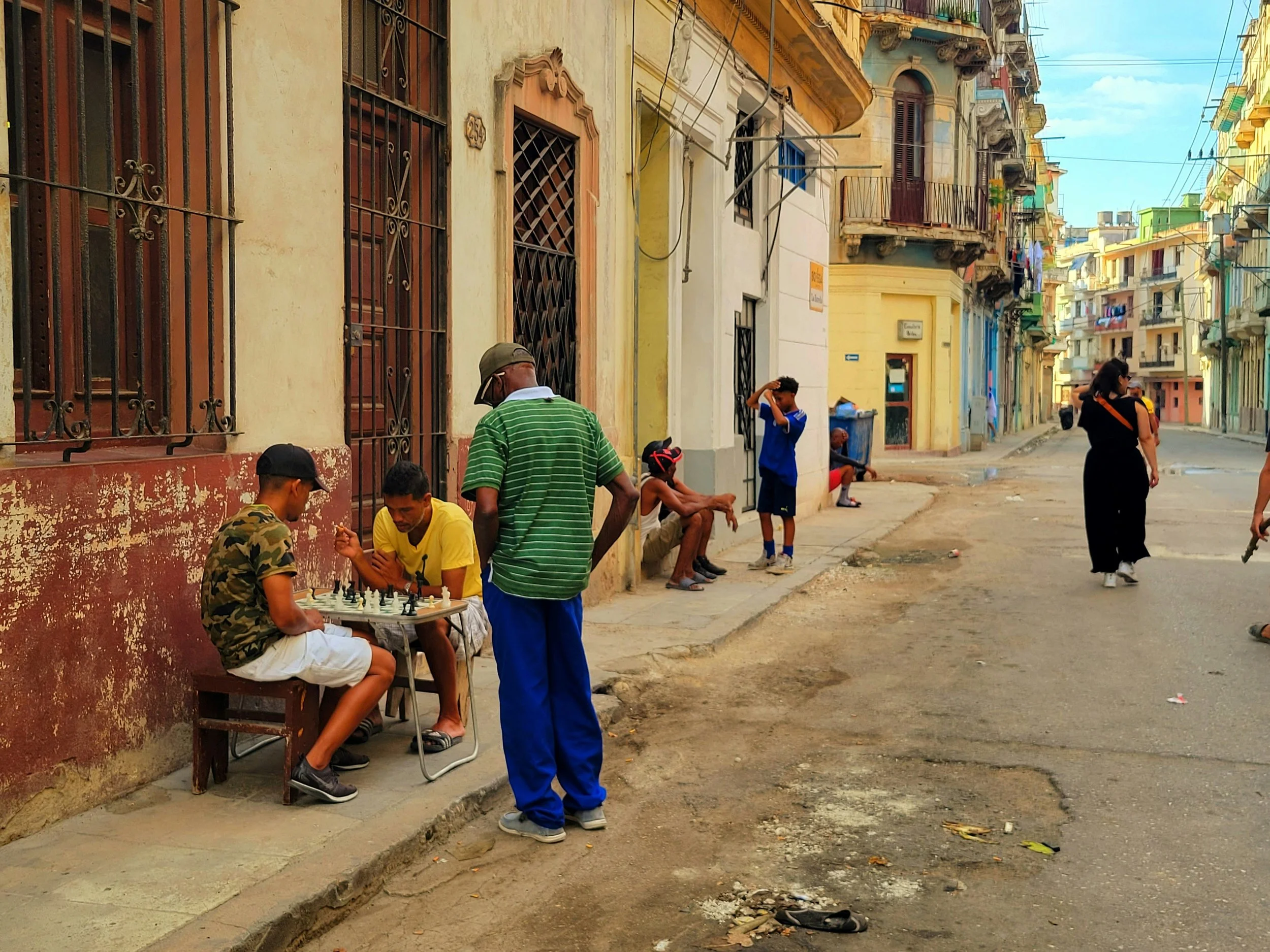 Local residents playing chess on a Havana sidewalk as daily life unfolds around them