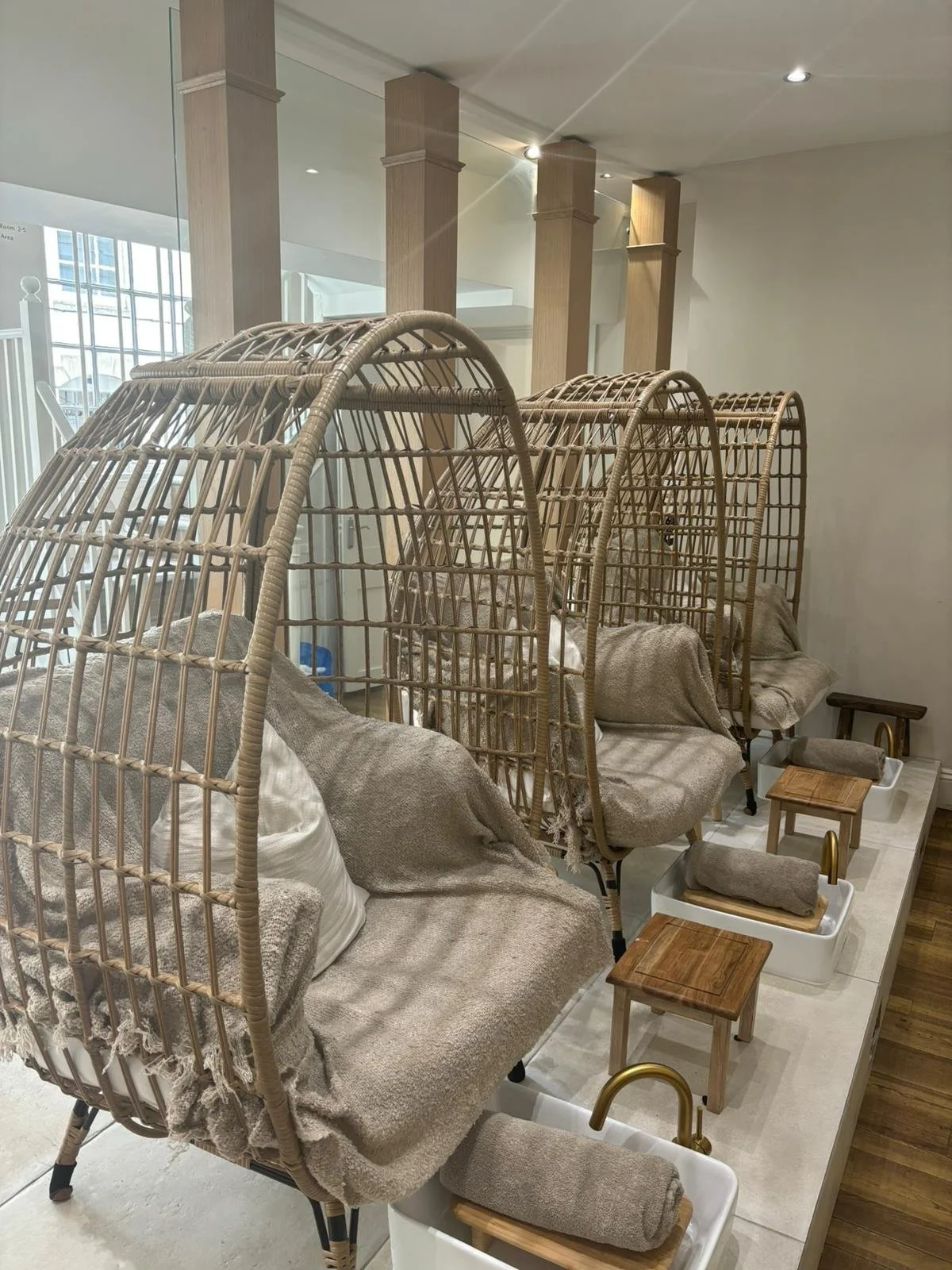 Three massage chairs with protective wicker coverings in a wellness or spa center, each with a towel and pillow, and small wooden and white foot baths with towels in front.