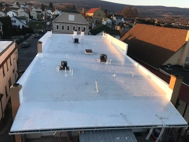 View of a flat commercial rooftop with four HVAC units, surrounded by residential houses and hills in the background during late afternoon or early evening.
