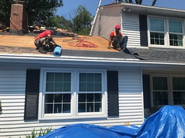 Two workers on a house roof, wearing safety gear and working on roofing and insulation.