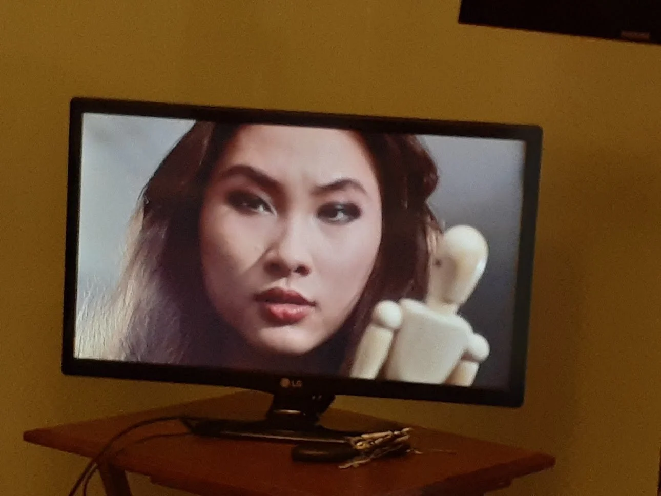 A woman looking at a small wooden mannequin on a TV screen.