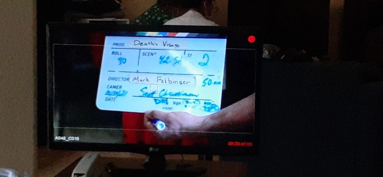 Photo of a television screen displaying handwritten notes for a death scene, including details like scene, scene number, director, camera, and date.
