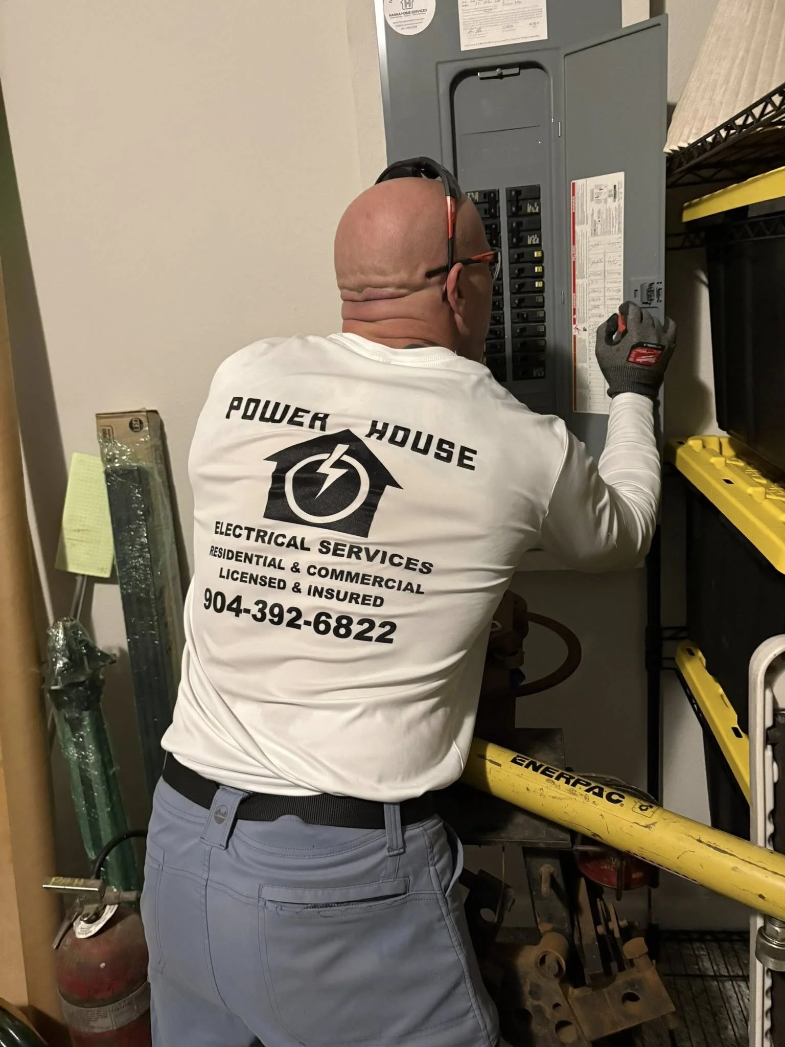 Man working on electrical panel in a utility room wearing a white shirt and gray pants.