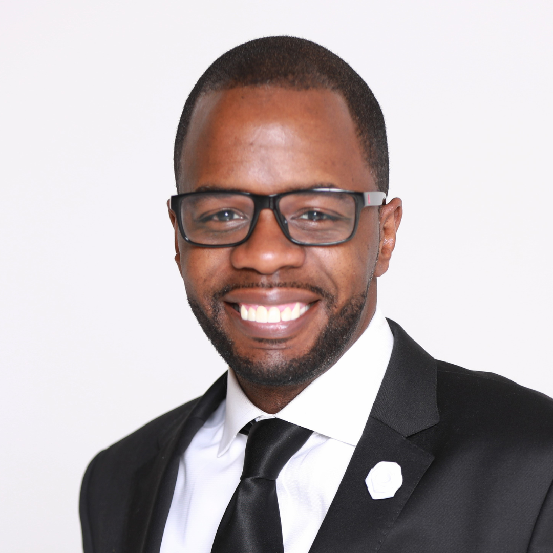 Professional headshot of a smiling man with glasses wearing a black suit and tie, on a white background.