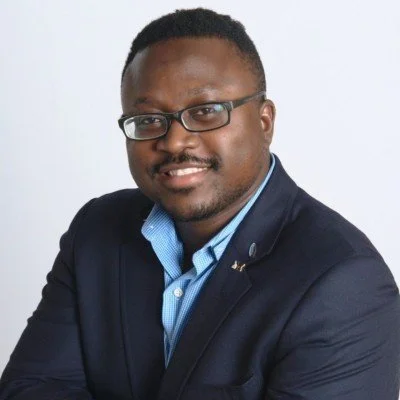 Professional portrait of a man in a dark suit and glasses smiling at the camera.
