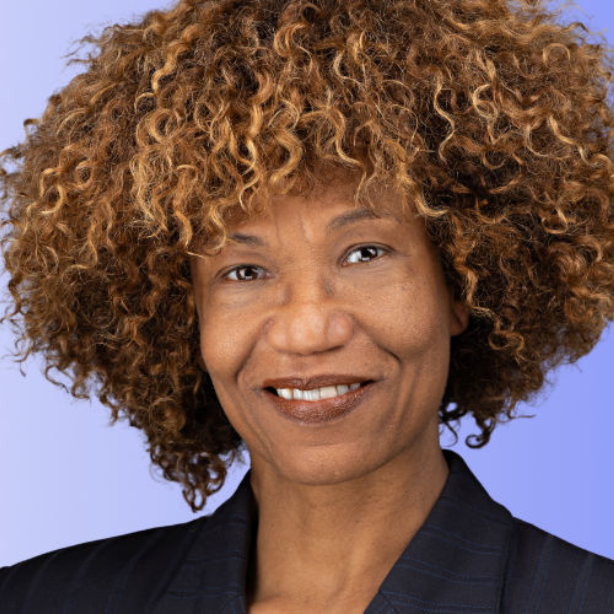 Close-up of a woman's face with curly, reddish-brown hair and a smile, wearing a black top.