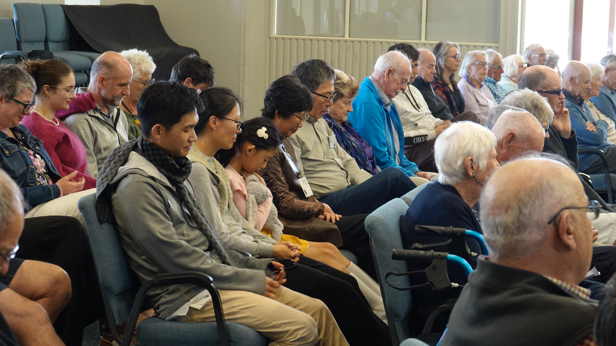 A large group of people at St Andrews church sitting with their heads bowed in prayer or reflection during a church service.