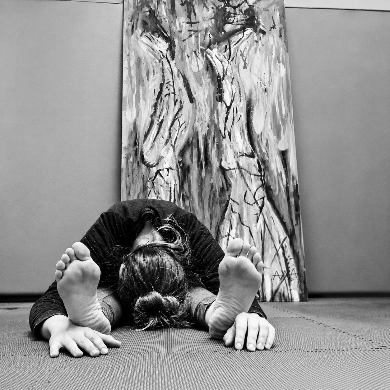 Persona haciendo una postura de yoga en el suelo, con un cuadro abstracto al fondo.
