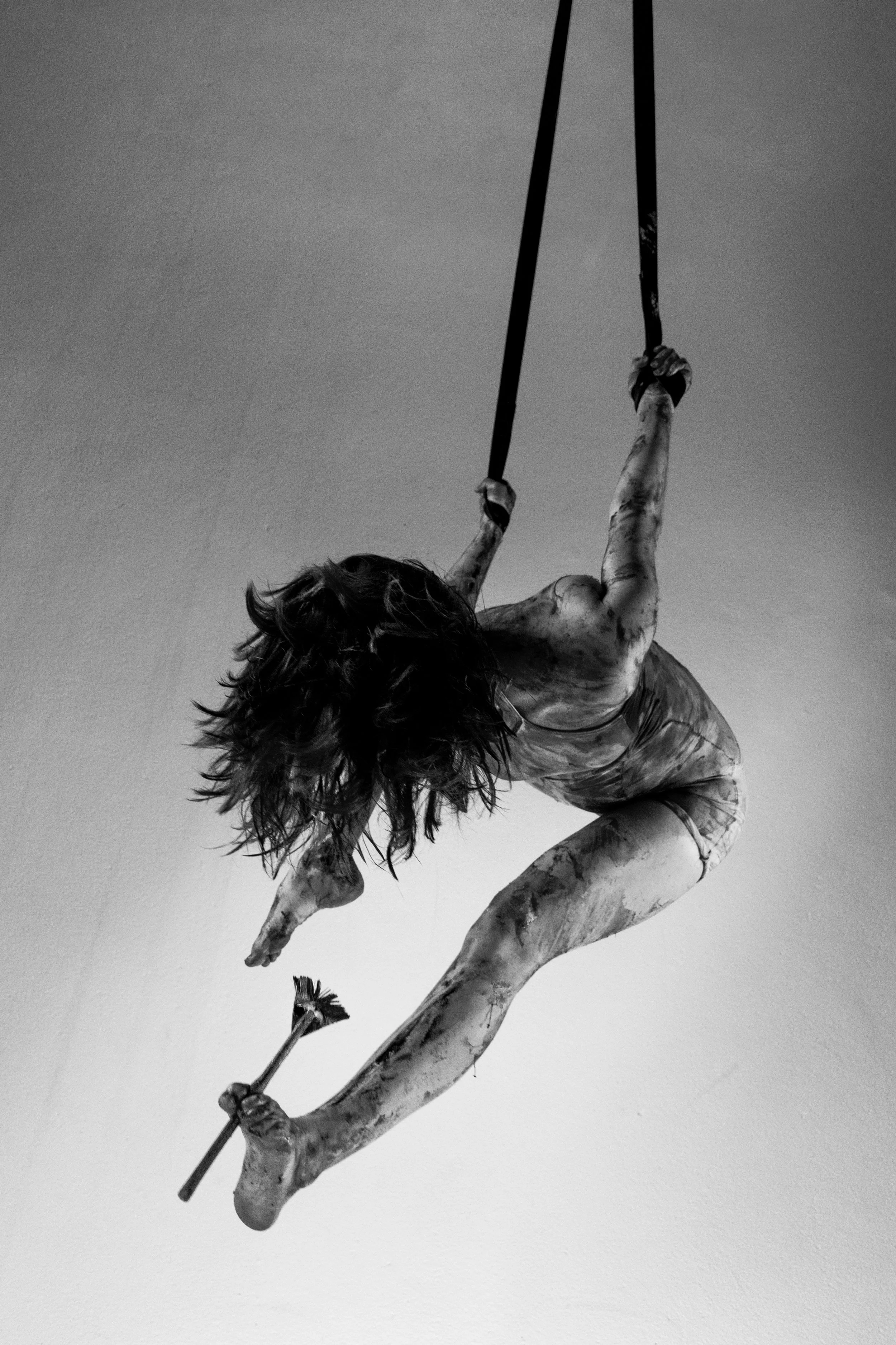 Escultura en blanco y negro de una figura femenina suspendida en el aire, sosteniéndose de una cuerda, con el cabello suelto y una rosa en la mano.
