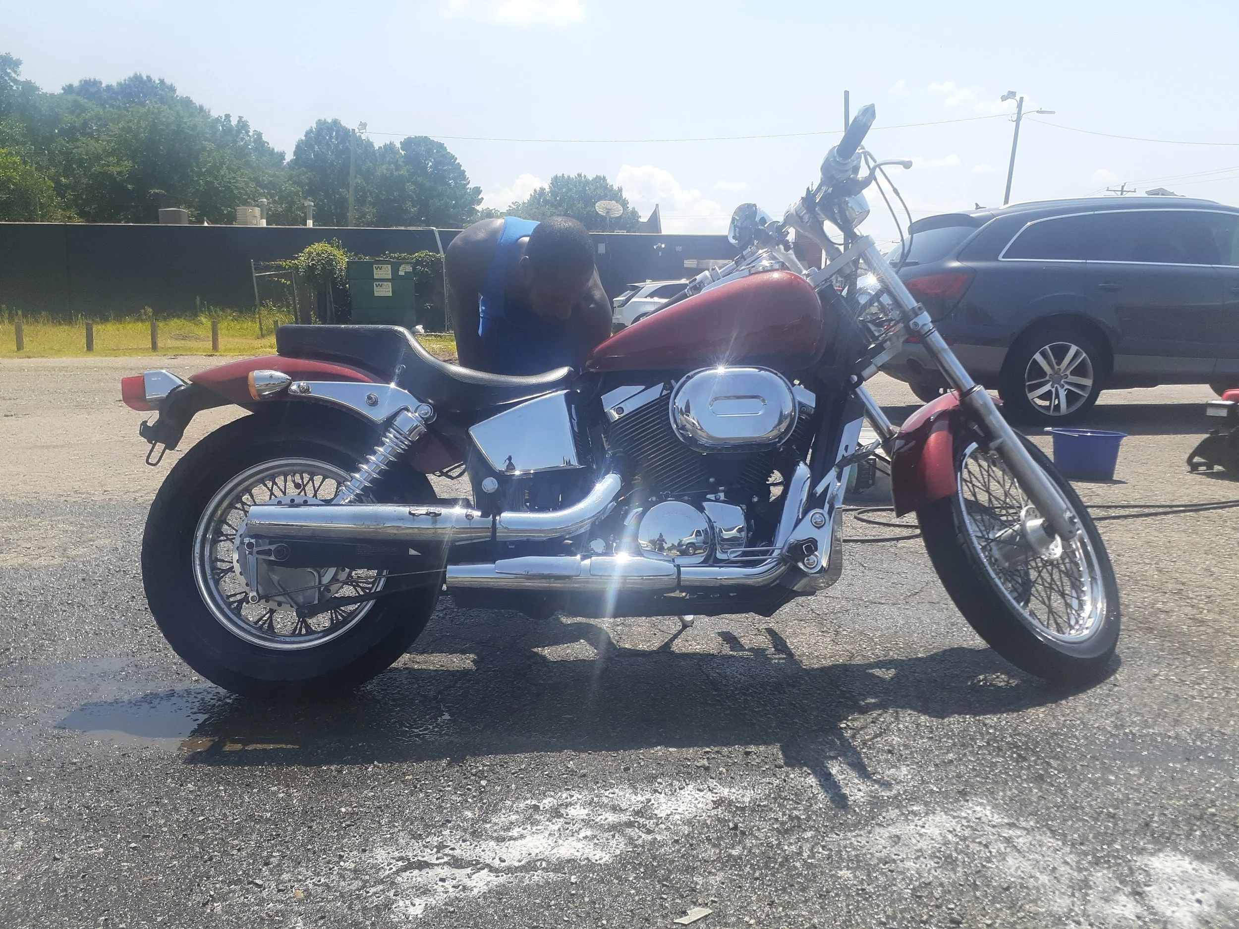 A red and chrome motorcycle parked on a street with parked cars and trees in the background.