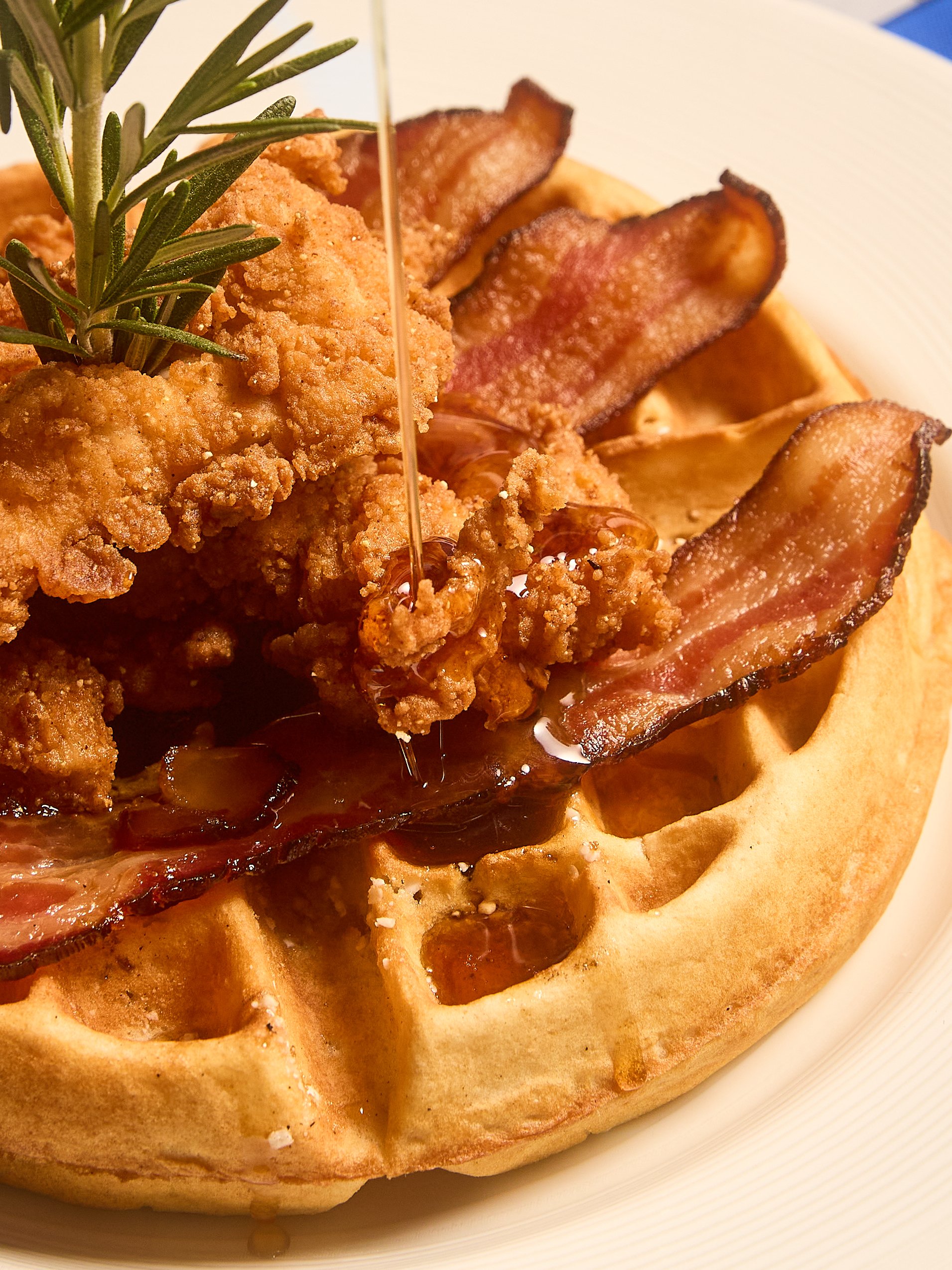 Close-up of a breakfast pizza topped with fried chicken, bacon, bacon jam, and garnished with a sprig of rosemary.