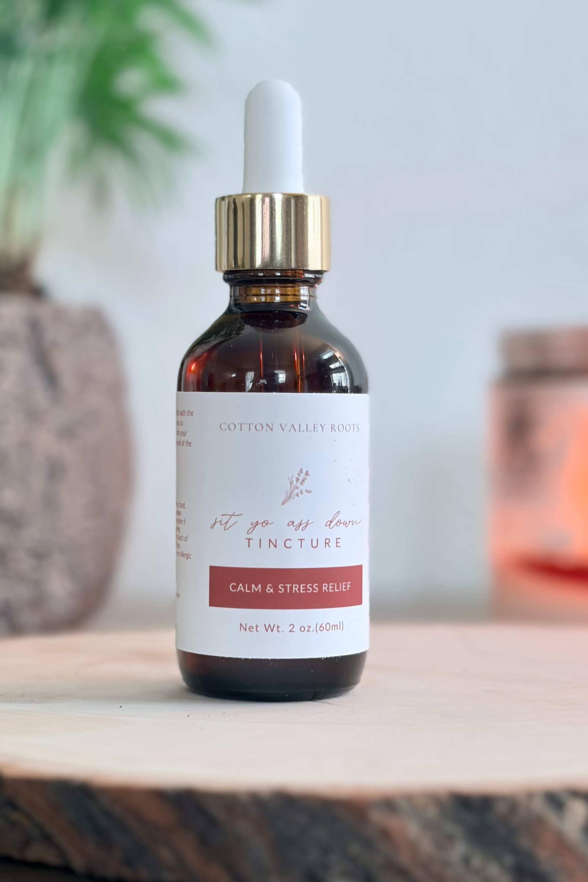 A small amber glass bottle with a white dropper cap containing tincture for calm and stress relief, labeled "Cotton Valley Roots".