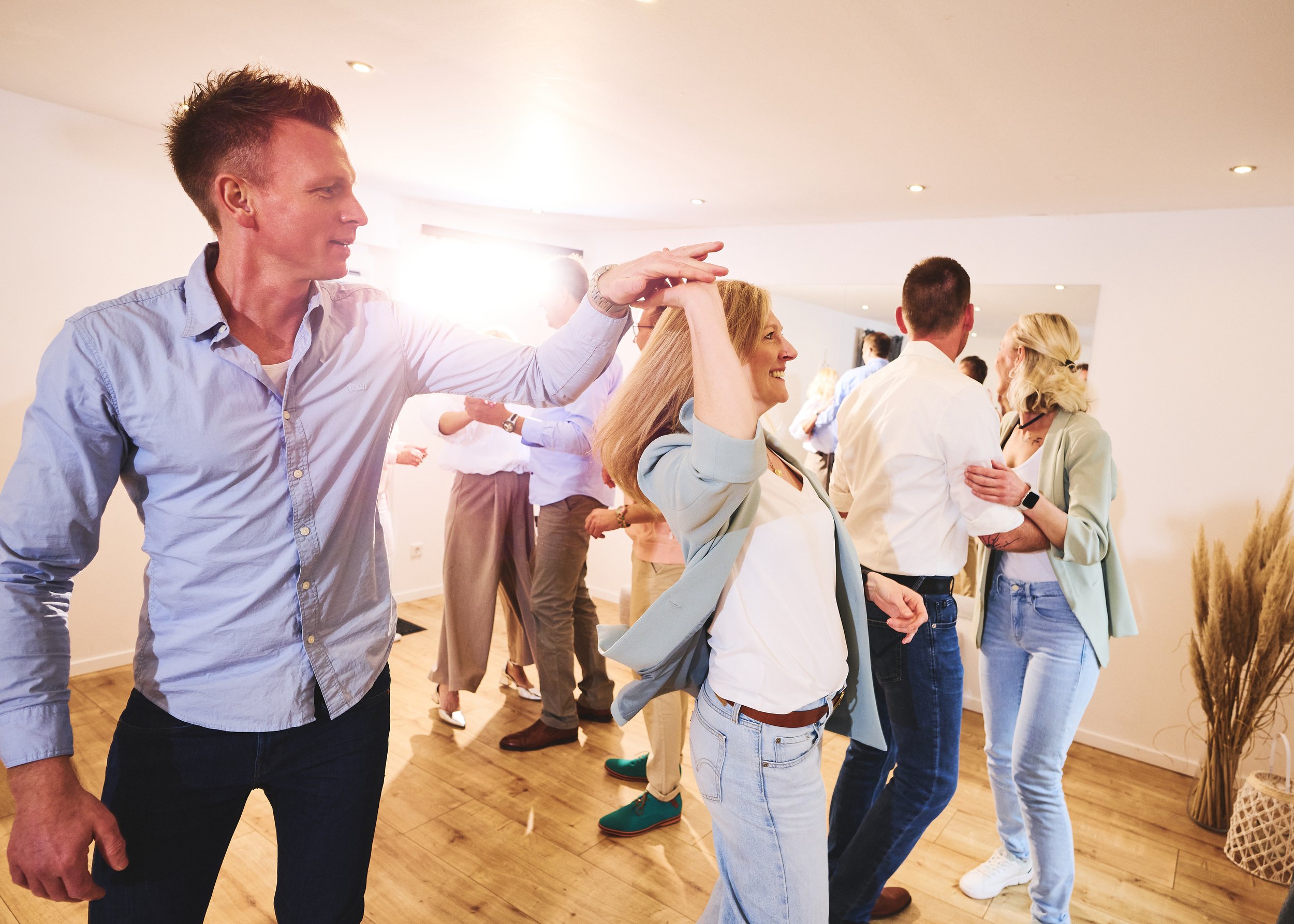 Menschen tanzen und lachen in einer hell erleuchteten, modernen Wohnung bei einer sozialen Zusammenkunft.