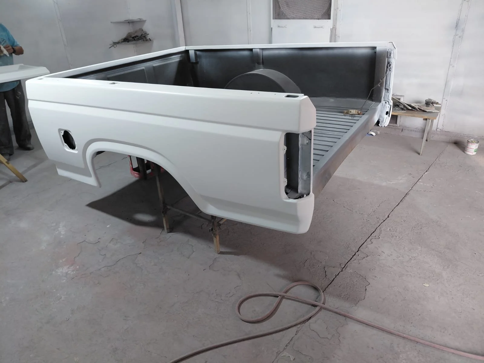 Pieza de carrocería de una camioneta en proceso de reparación o pintura en un taller, mostrada en un entorno industrial con paredes blancas y piso de concreto.