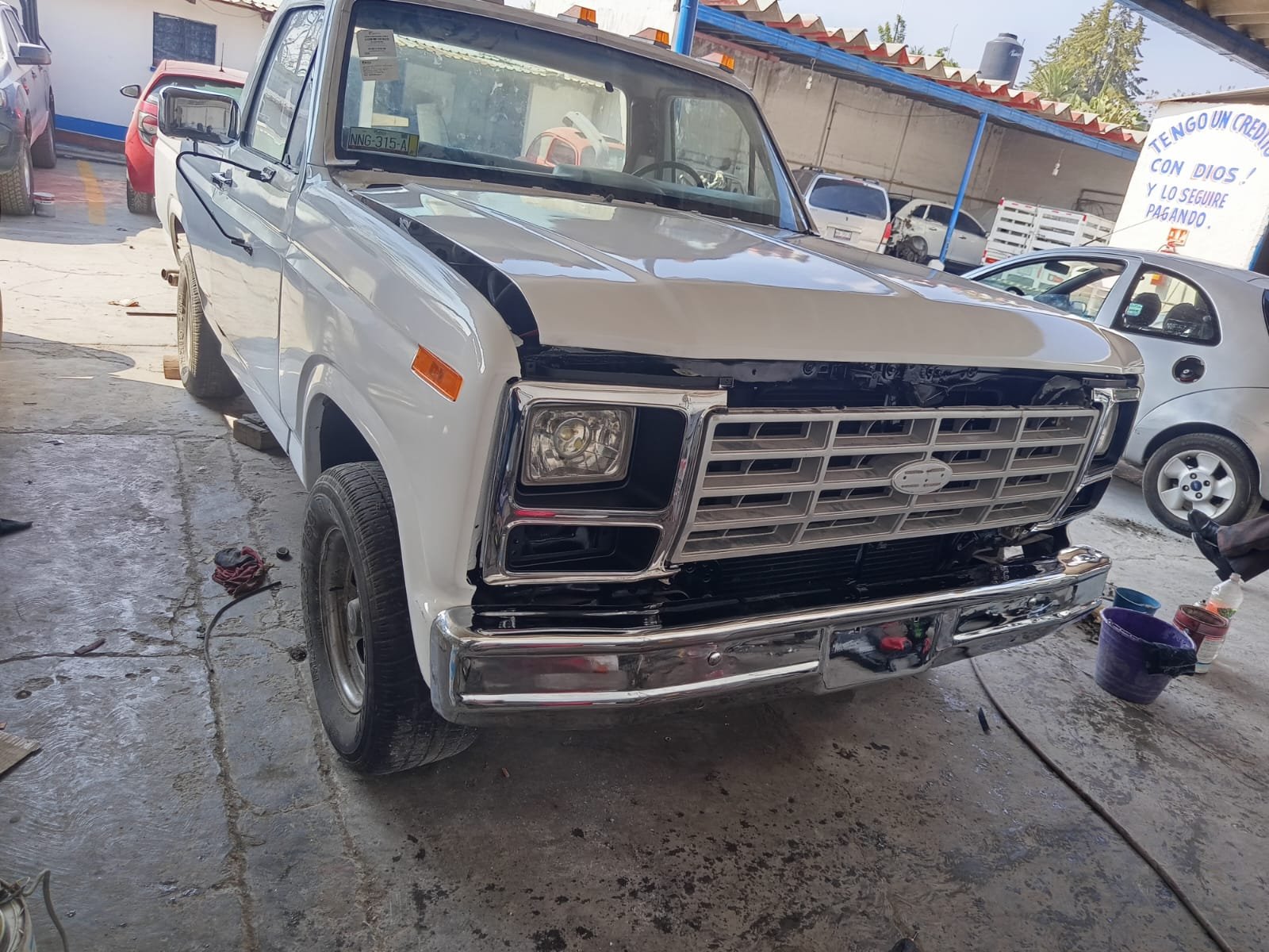 Autos en reparación, con uno en primer plano que todavía requiere trabajo en la parte delantera, en un taller o garaje.
