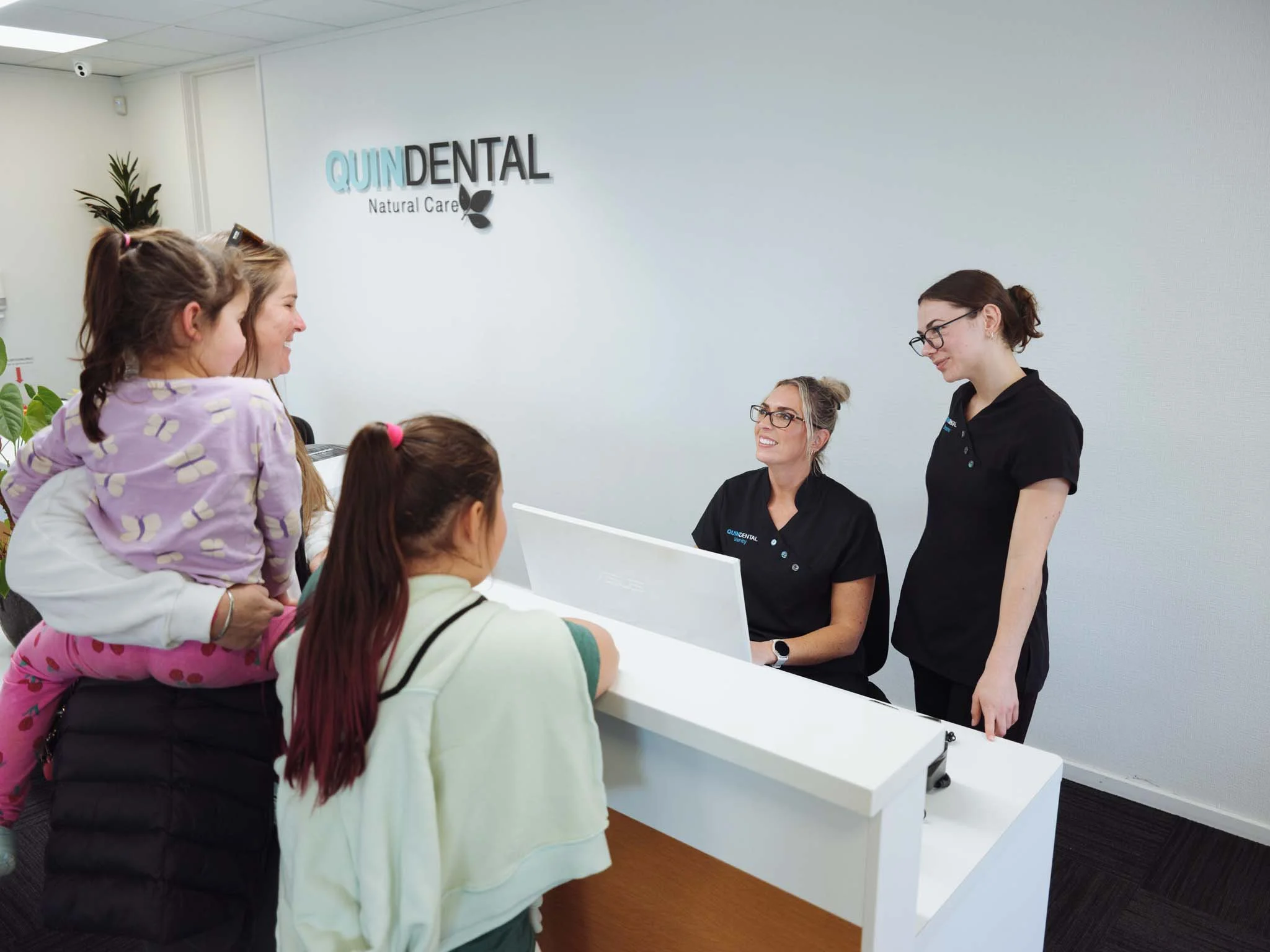 Reception area at Quin Dental, Nelson, New Zealand. Staff and children are engaging in conversation.