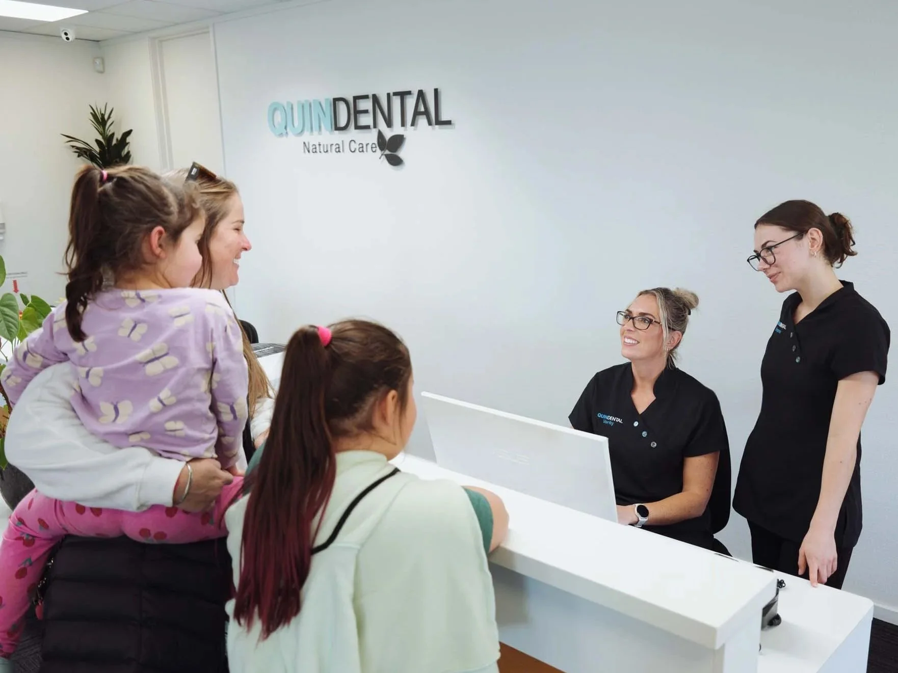 Reception area at Quin Dental, Nelson, New Zealand. Staff and children are engaging in conversation.