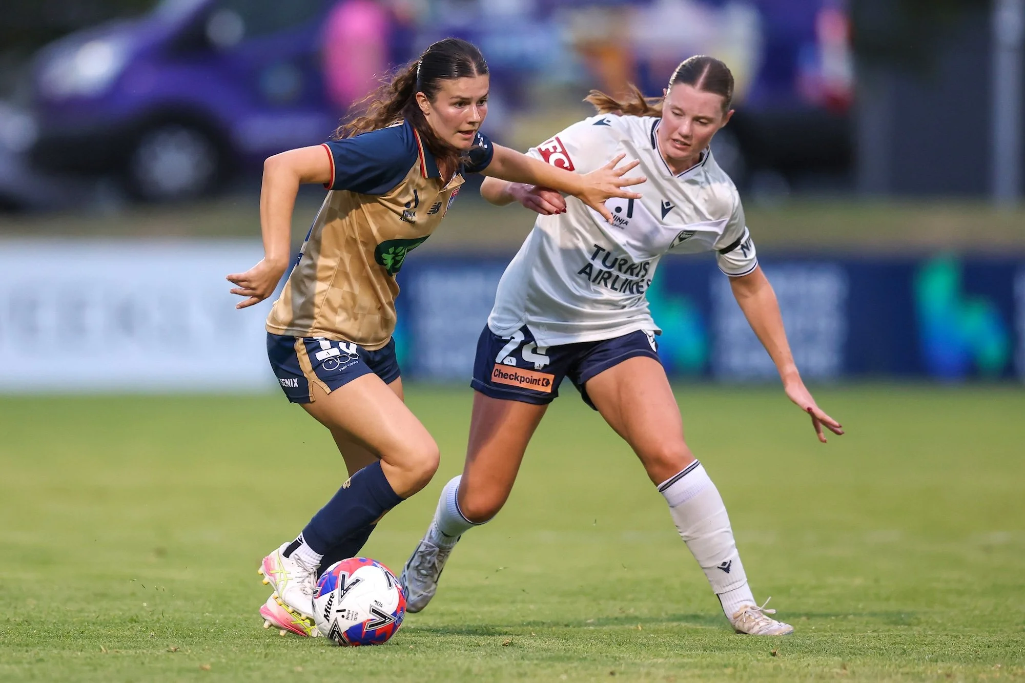 Two women's soccer players competing for the ball on a grass field during a match
