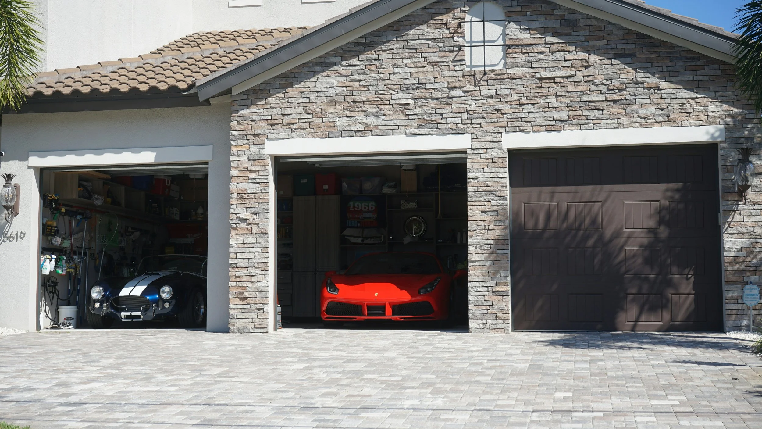 DOMUS Home Watch Services - Garage with two open doors, containing a black classic car on the left and a red sports car on the right, with storage shelves and items in the background.