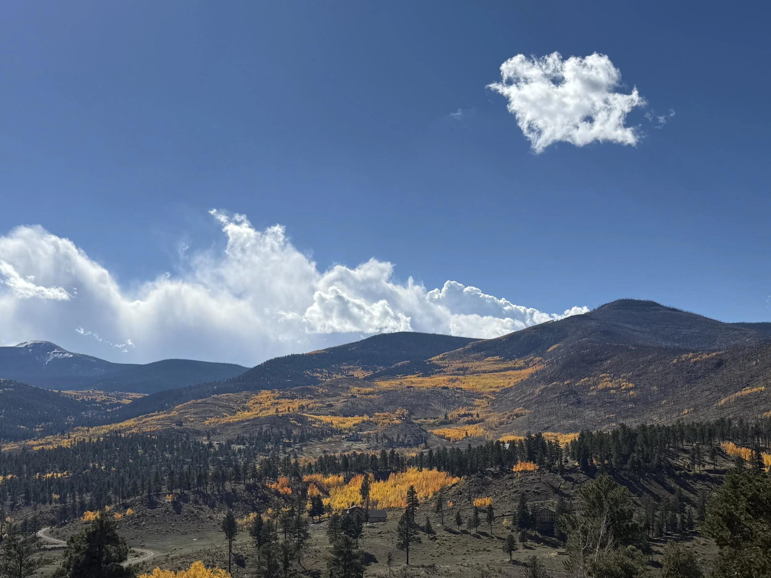 Mountains with colorful fall foliage under a blue sky with a cloud shaped like a heart.