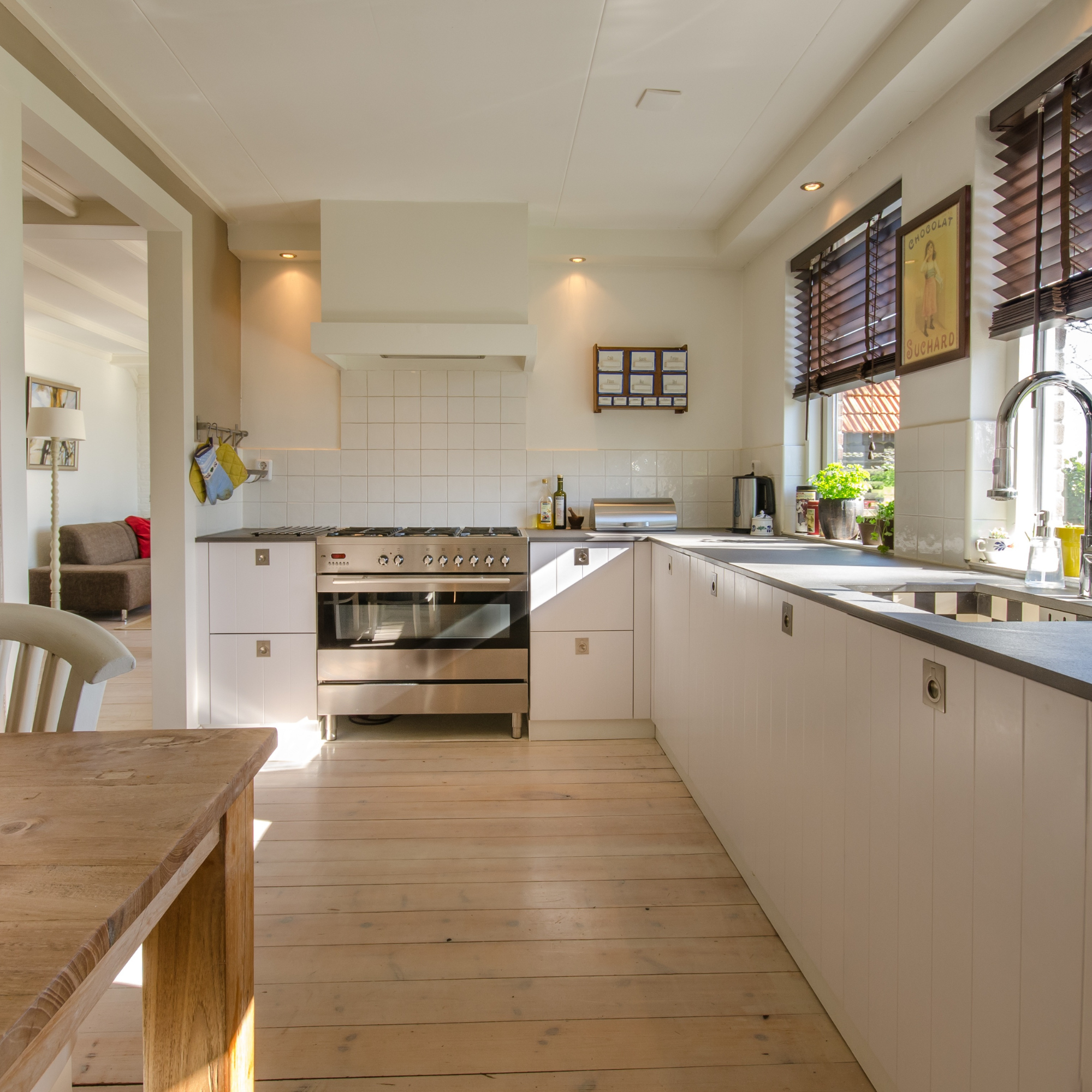Modern kitchen with white cabinets, cooking stove, wooden flooring, and window with blinds.