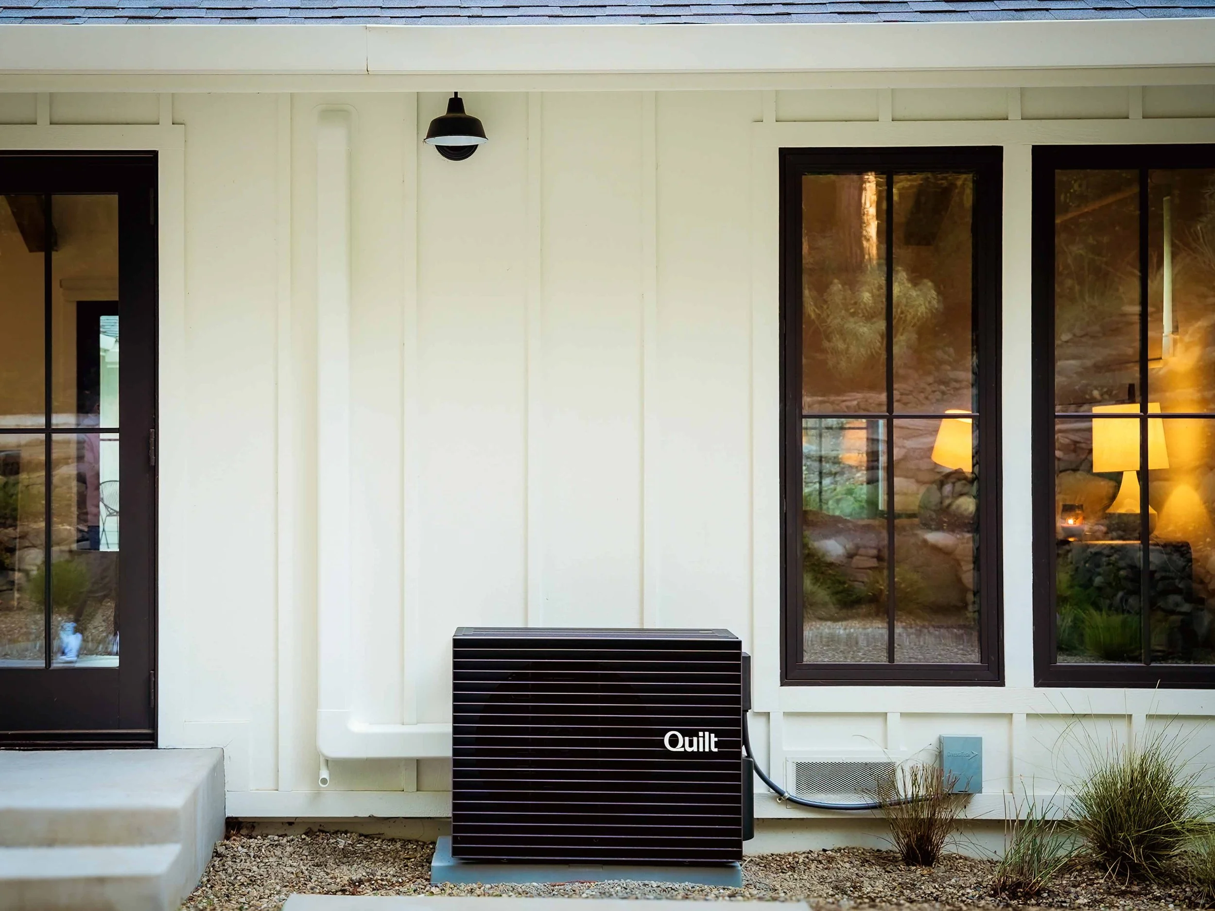 Sleek black Quilt outdoor heat pump unit installed cleanly next to a residential exterior wall.