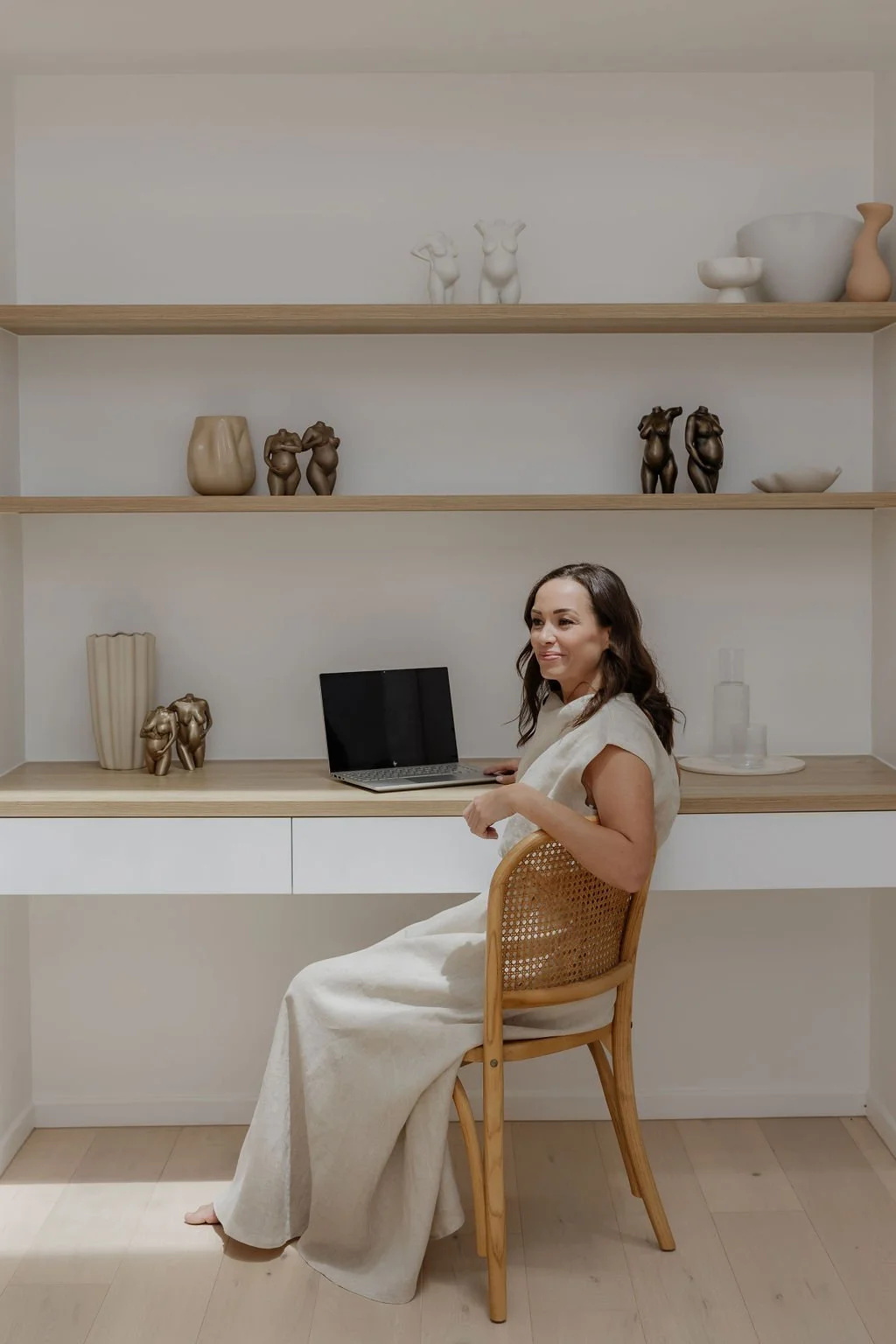 Libby, Founder of Sett & Maxe, in a room with minimalist decor and wooden shelves holding abstract sculptures and vases.