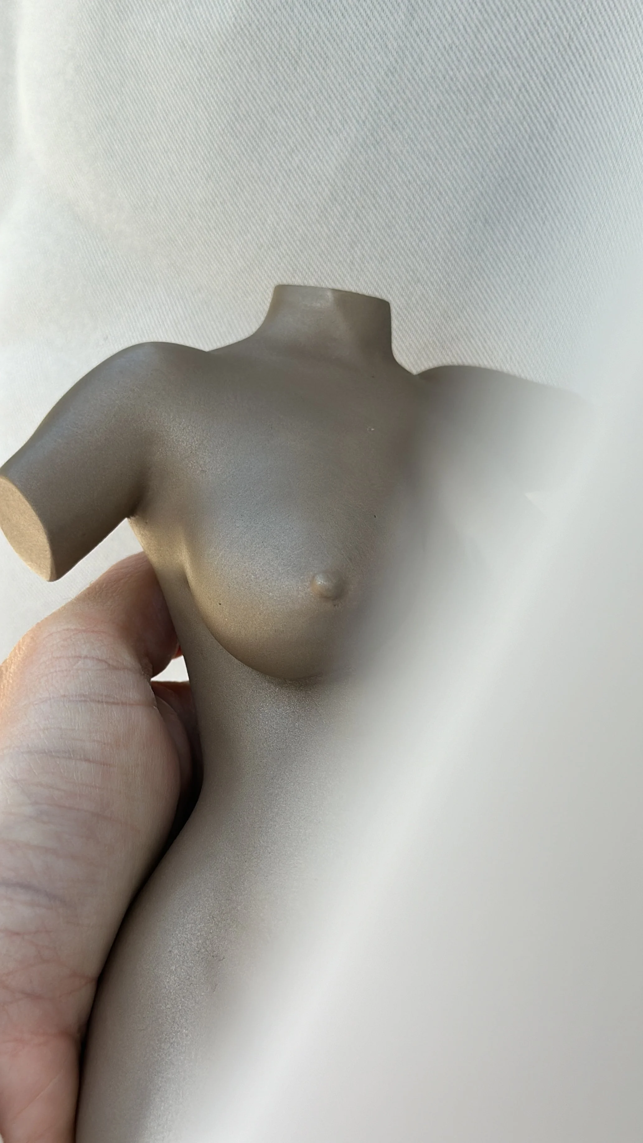 A hand holding a small, beige, pregnancy statue