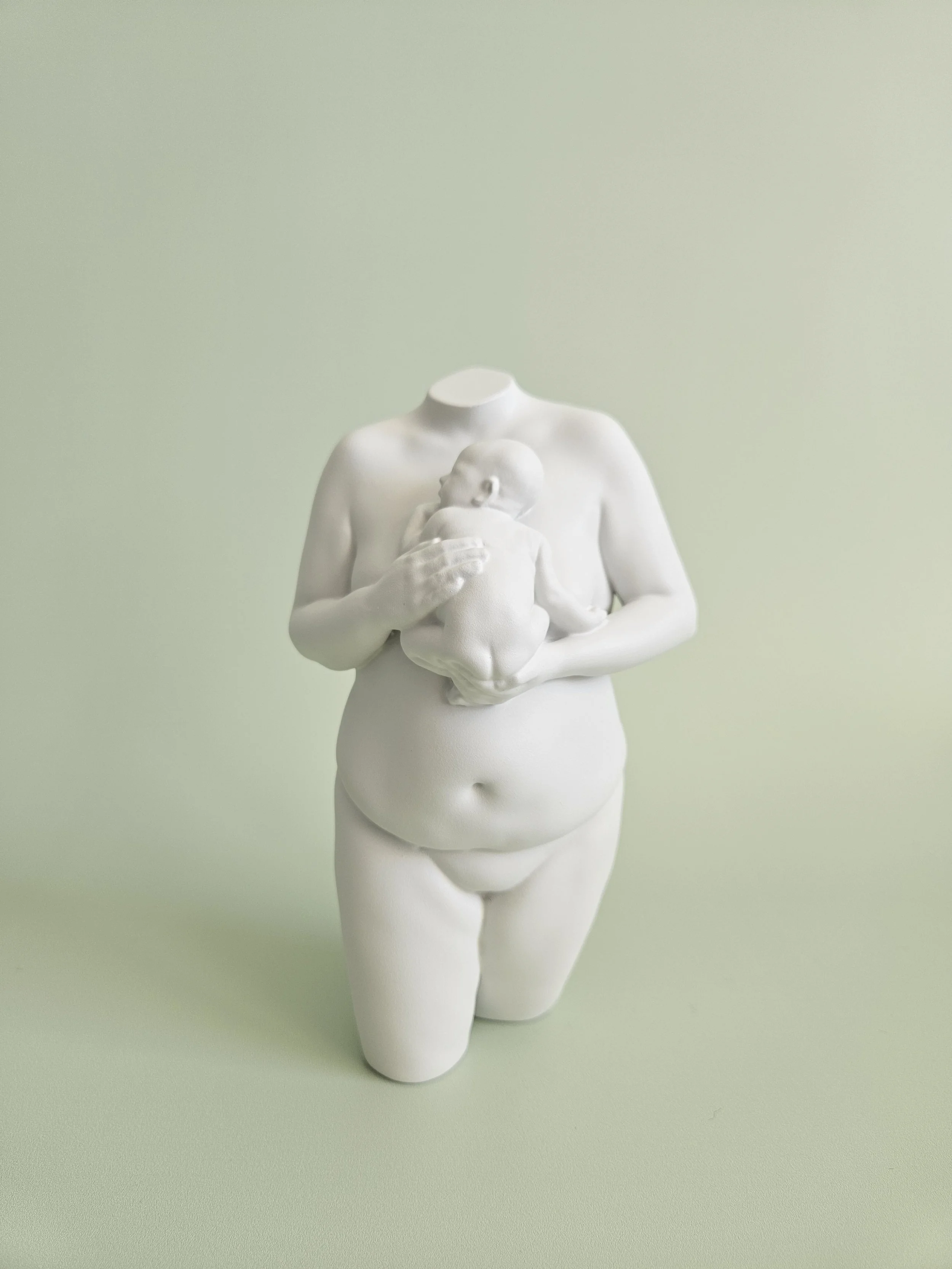 A white sculpture of a pregnant woman holding a baby against a light green background.