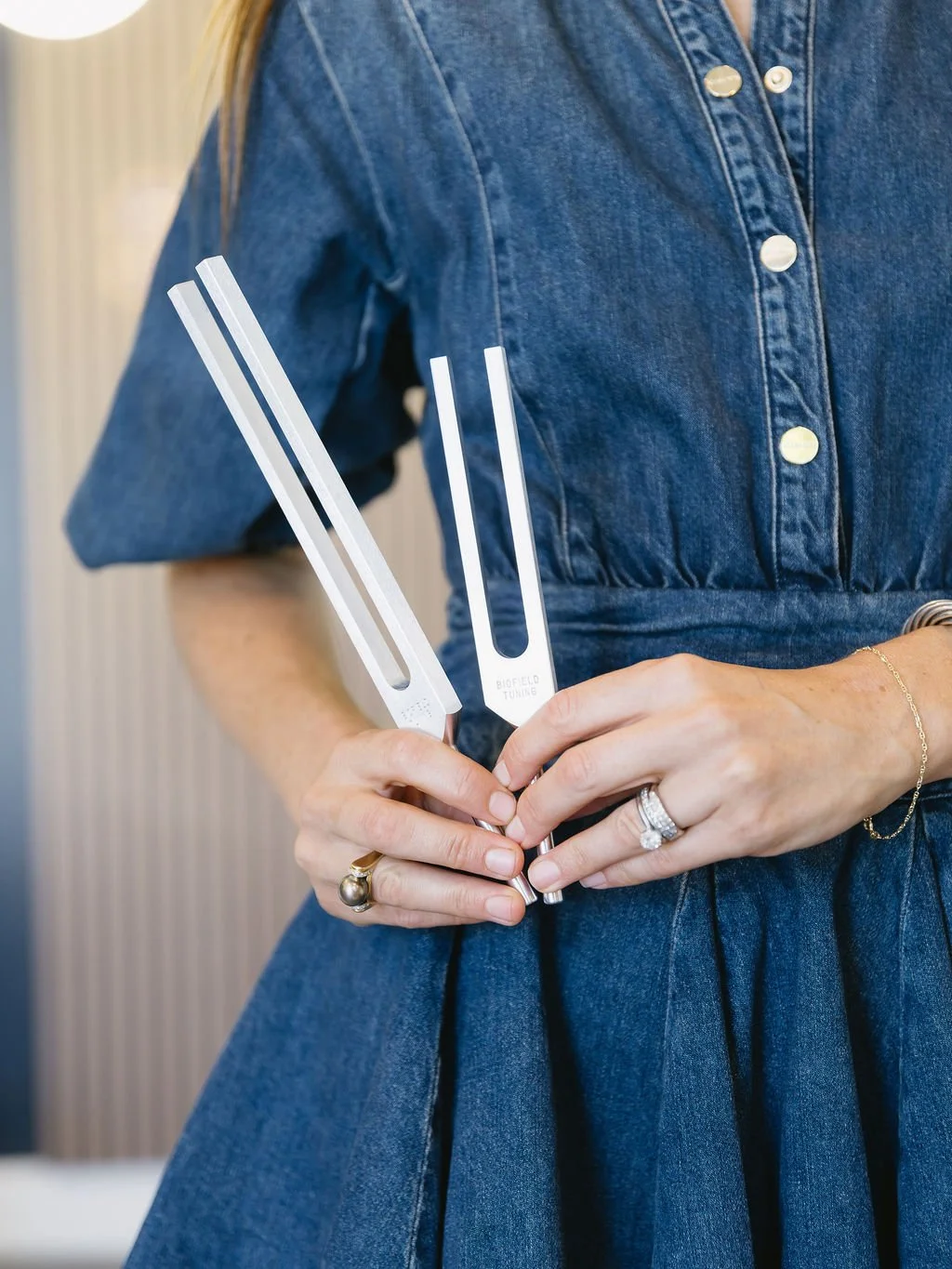 A woman wearing a denim dress holding two tuning forks in her hands.