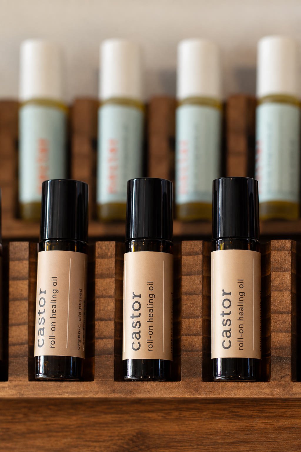 Three small bottles of castor roll-on healing oil with black caps, placed on a wooden shelf with additional bottles in the background.