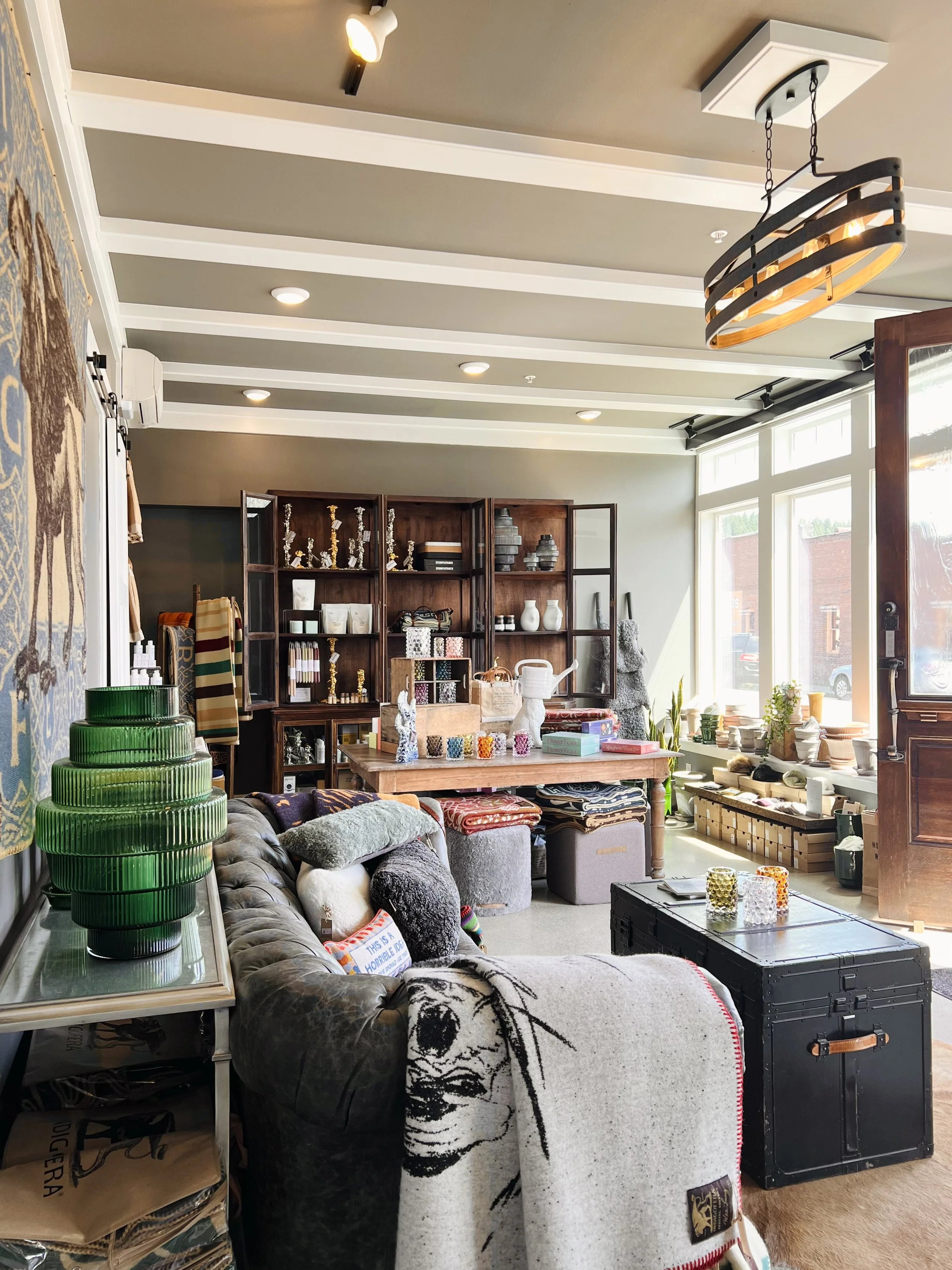 The lobby boutique at Hotel Roslyn in Roslyn, WA. Interior of a boutique store with display shelves of home decor items, a sofa with pillows, a coffee table, and a large window letting in natural light.