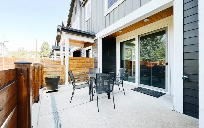 A patio area with a dining table and chairs, surrounded by a wooden fence and gray siding on the building.
