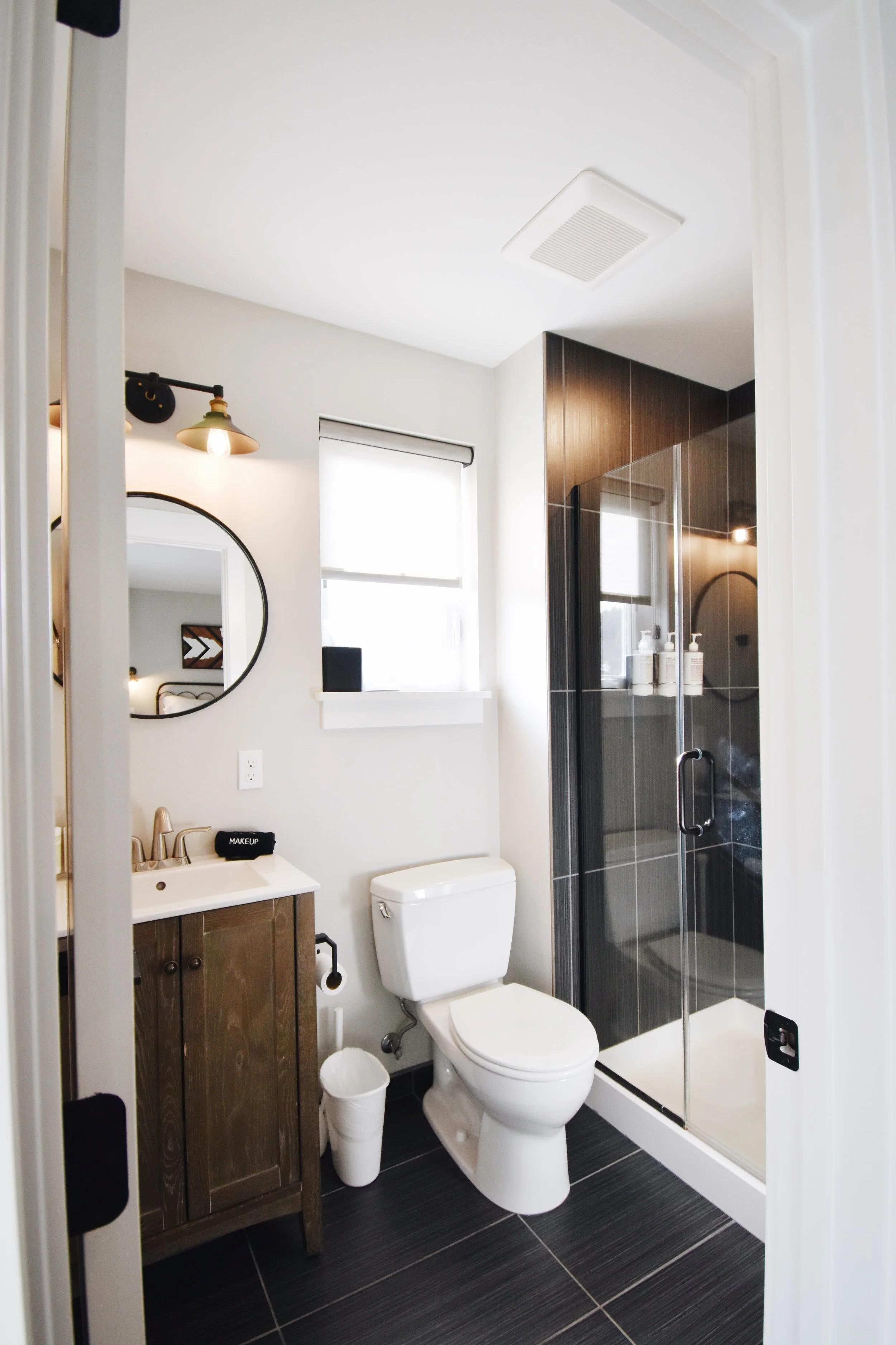 A modern bathroom with a toilet, shower, sink, and mirror.