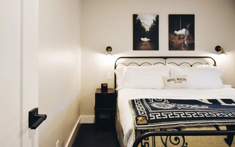 A 2nd Floor King Suite room at Hotel Roslyn, in Roslyn, WA. A cozy hotel bedroom with a double bed, decorative pillows, and a black and gold throw blanket. 