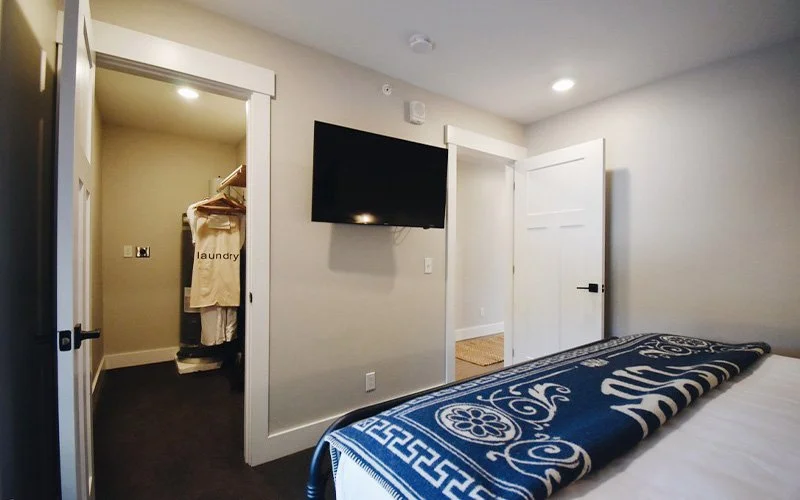 A 2nd Floor King Suite room at Hotel Roslyn, in Roslyn, WA. A bedroom with an unmade bed, a wall-mounted flat-screen TV, and a laundry closet with a shirt hanging.