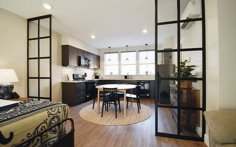 A King Patio room at Hotel Roslyn in Roslyn, WA. Open-concept kitchen and dining area with black cabinets, round wooden dining table, four black chairs, and large windows.