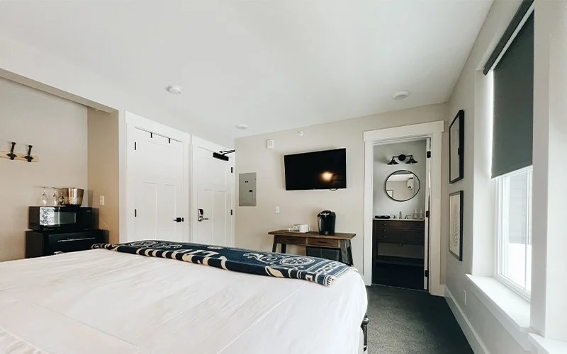 A wide view of a hotel room with a bed, TV, window, and bathroom door open