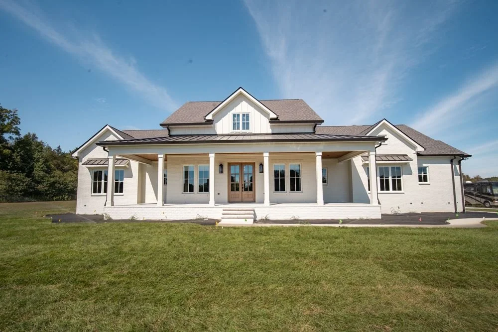 Front of a white custom home in Lebanon, TN with a full-width covered front porch, columns and wood front doors