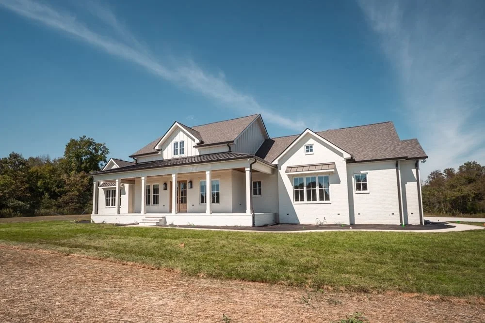 Corner view of a white two-story custom home with gabled rooflines and a covered porch on an open lot