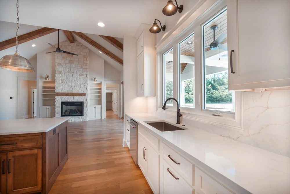 Kitchen sink under a row of windows with white cabinets, wall sconces and a view to the living room fireplace