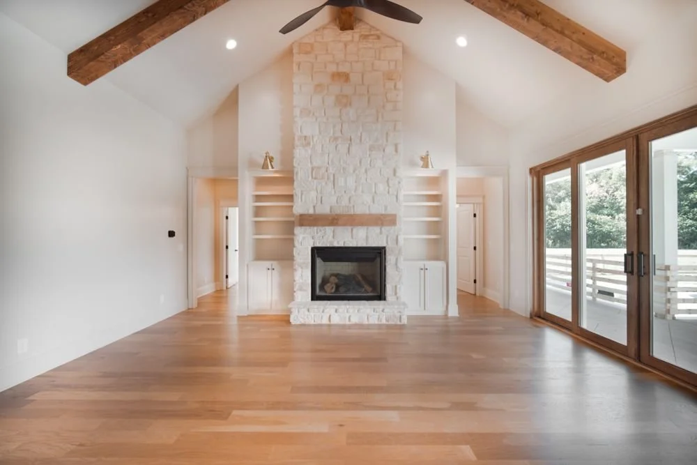 Vaulted living room with exposed wood beams, a floor-to-ceiling stone fireplace, built-in shelves and glass sliding doors