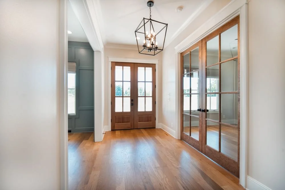 Entry hall with a lantern light, wood front doors and glass-paneled wood doors to a side room