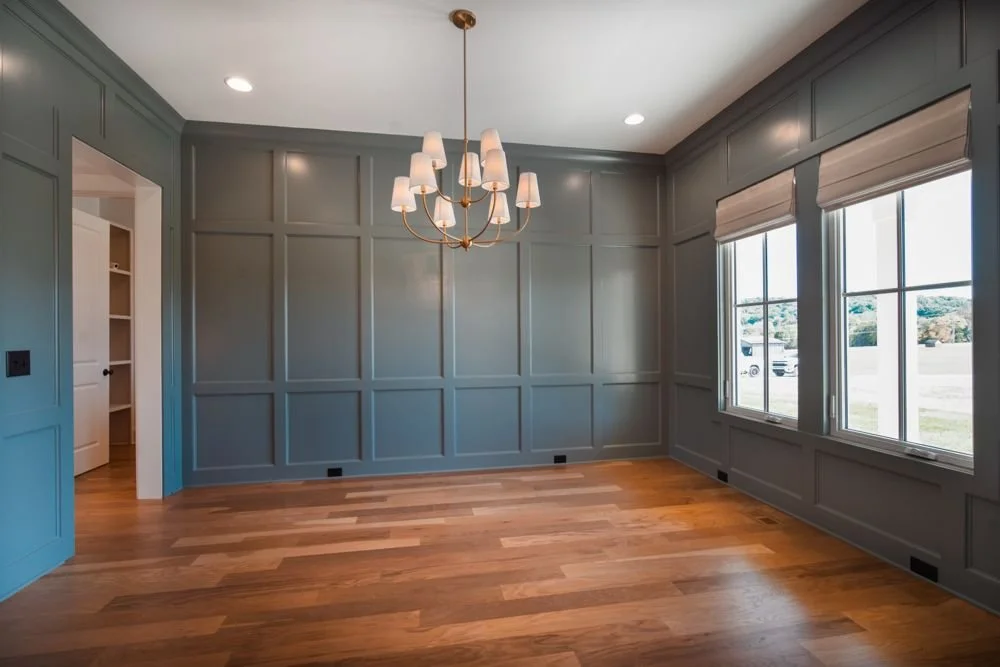 Dining room with blue-gray paneled walls, a chandelier and two windows